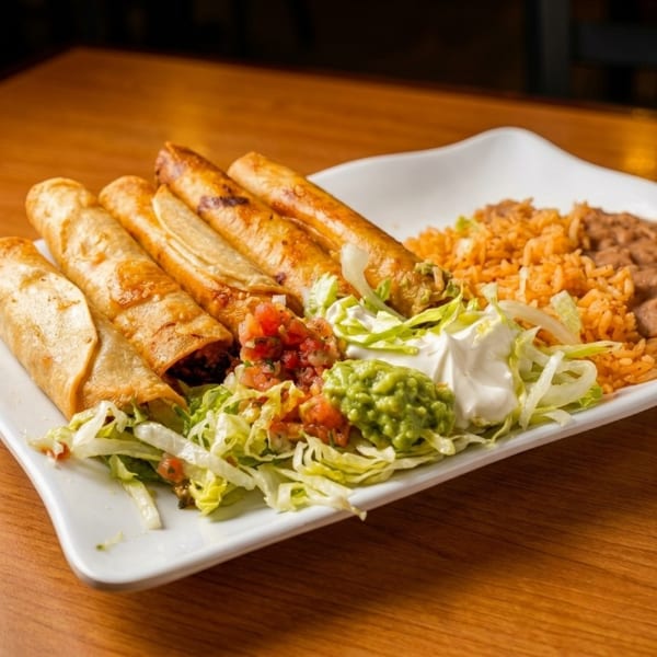 A plate of golden taquitos with rice, beans, guacamole, salsa, sour cream, and shredded lettuce.